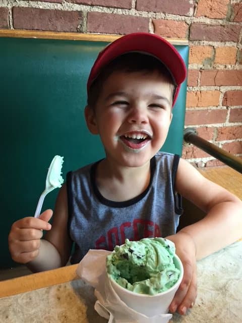 Jacob laughing with mint ice cream around his mouth, a spoon in one hand and a cup of ice cream in the other.