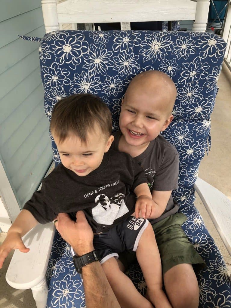 Jacob laughs on a blue floral porch chair with a younger sibling sitting on his lap.