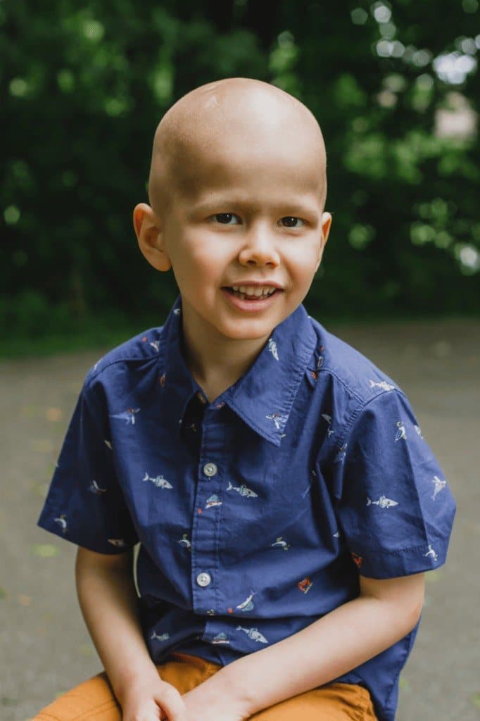 Jacob smiling outdoors in a blue shirt printed with small fish, green trees behind him.
